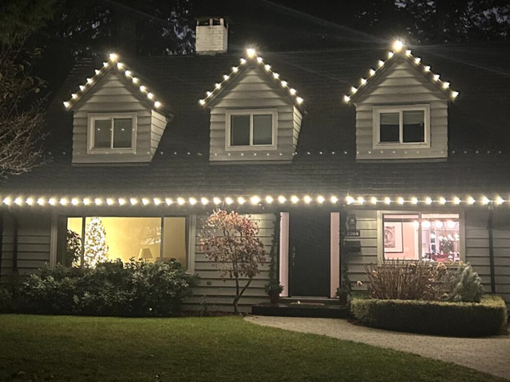 The same house at night with warm white lights along every roofline and dormer